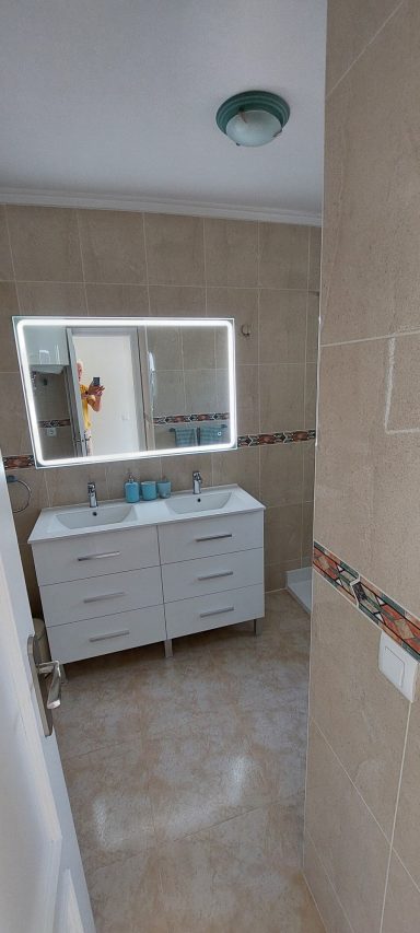 Moderne badkamer met witte wastafel en grote spiegel, lichte tegels en neutralen kleuren.