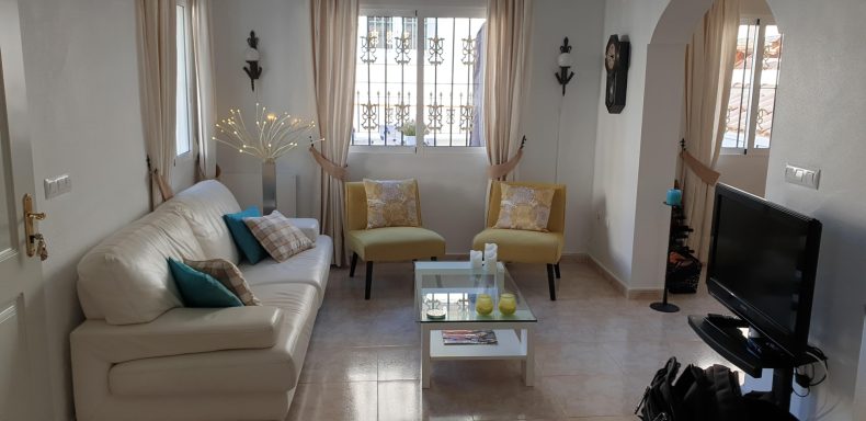 Een lichte woonkamer met een bank, twee gele stoelen en een tv. Decor met planten.