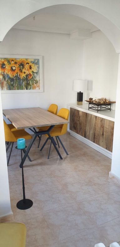 Eettafel met gele stoelen in lichte, moderne ruimte met zonnebloemen aan de muur.